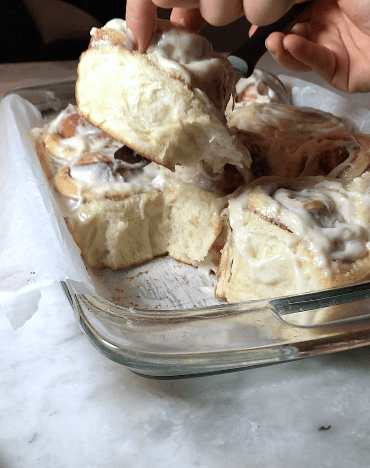 Fresh cinnamon roll getting pulled out of the pan, showing its fluffy, soft and stringy texture