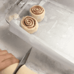 Cinnamon rolls in a log, getting sliced and placed into a baking tray