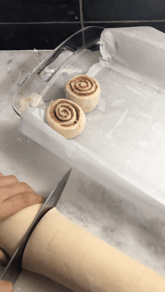 Cinnamon rolls in a log, getting sliced and placed into a baking tray