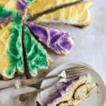 king cake sliced into pieces with one slice on a plate with forks