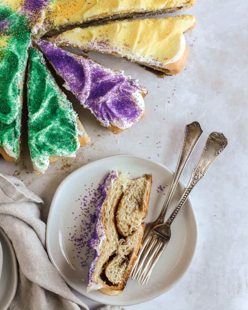king cake sliced into pieces with one slice on a plate with forks