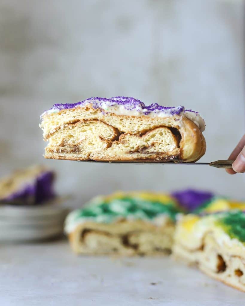 a slice of king cake suspended over a larger cake