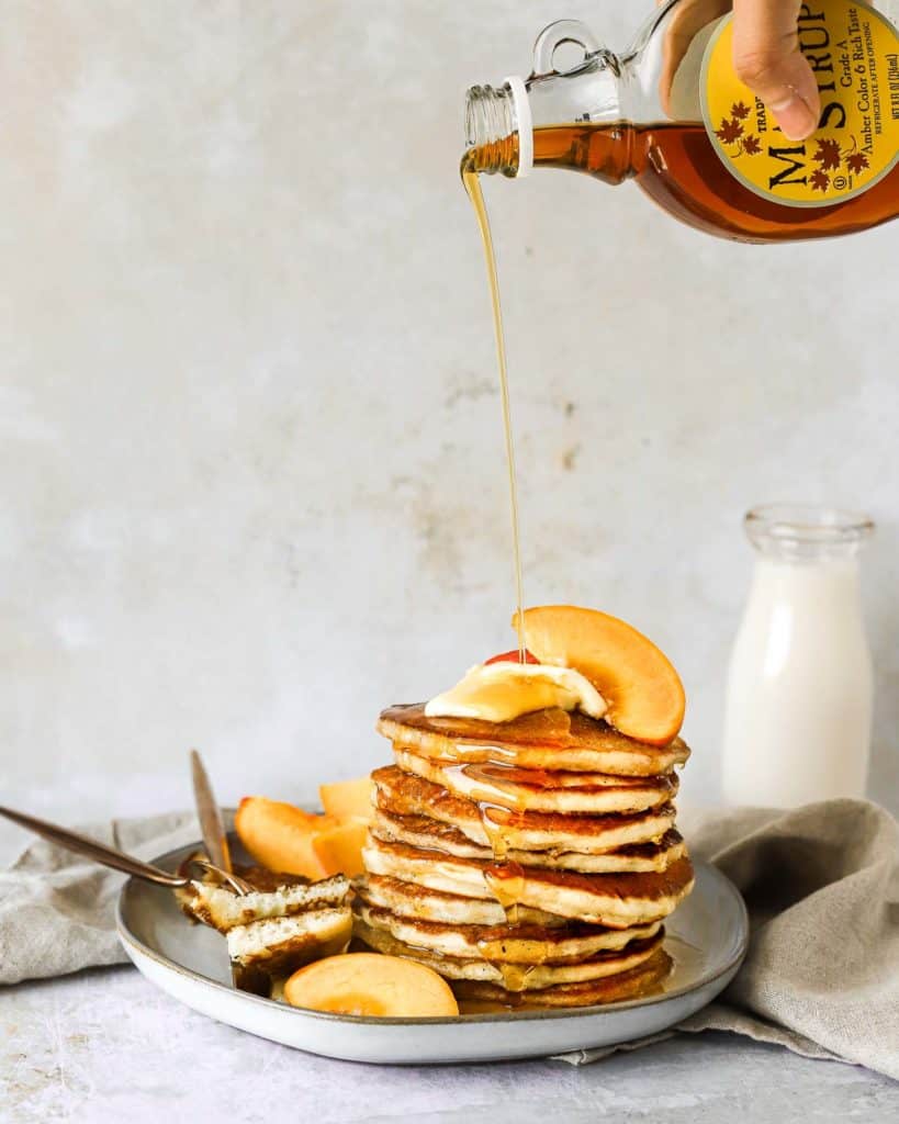 buttermilk pancakes on a plate with peaches and maple syrup
